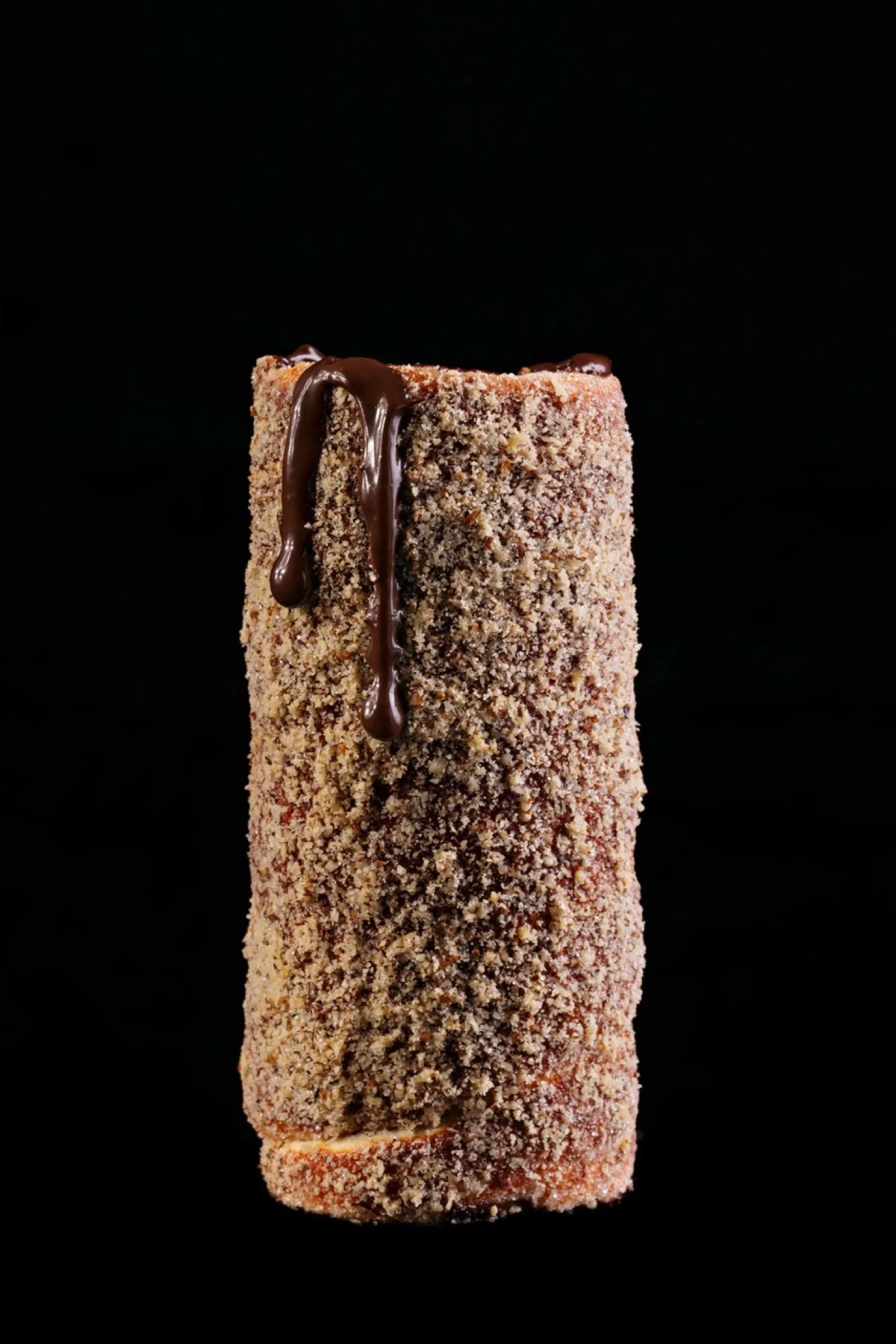 A walnut chimney cake with dark chocolate dripping down its side