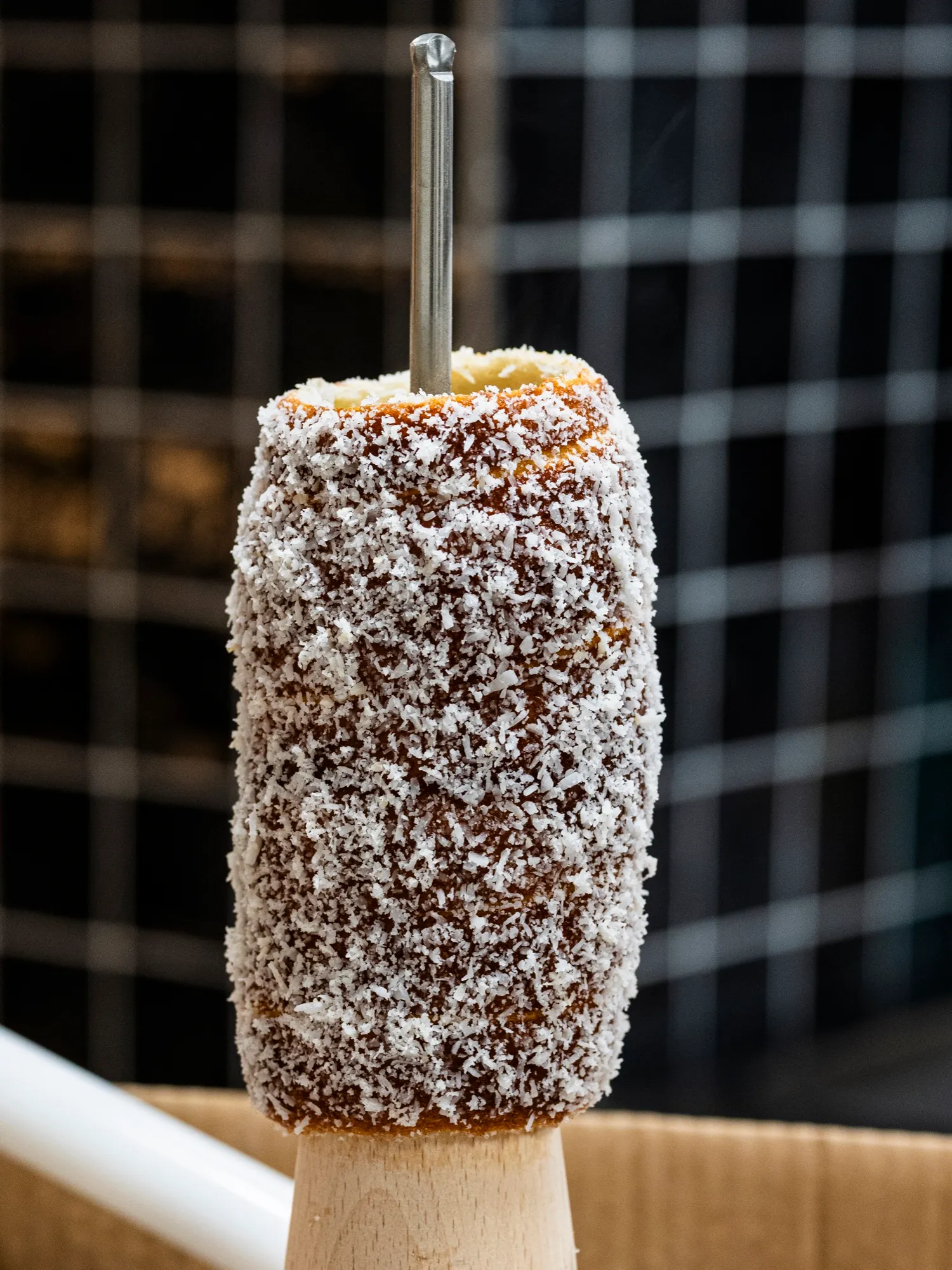A chimney cake coated in shredded coconut on the spit