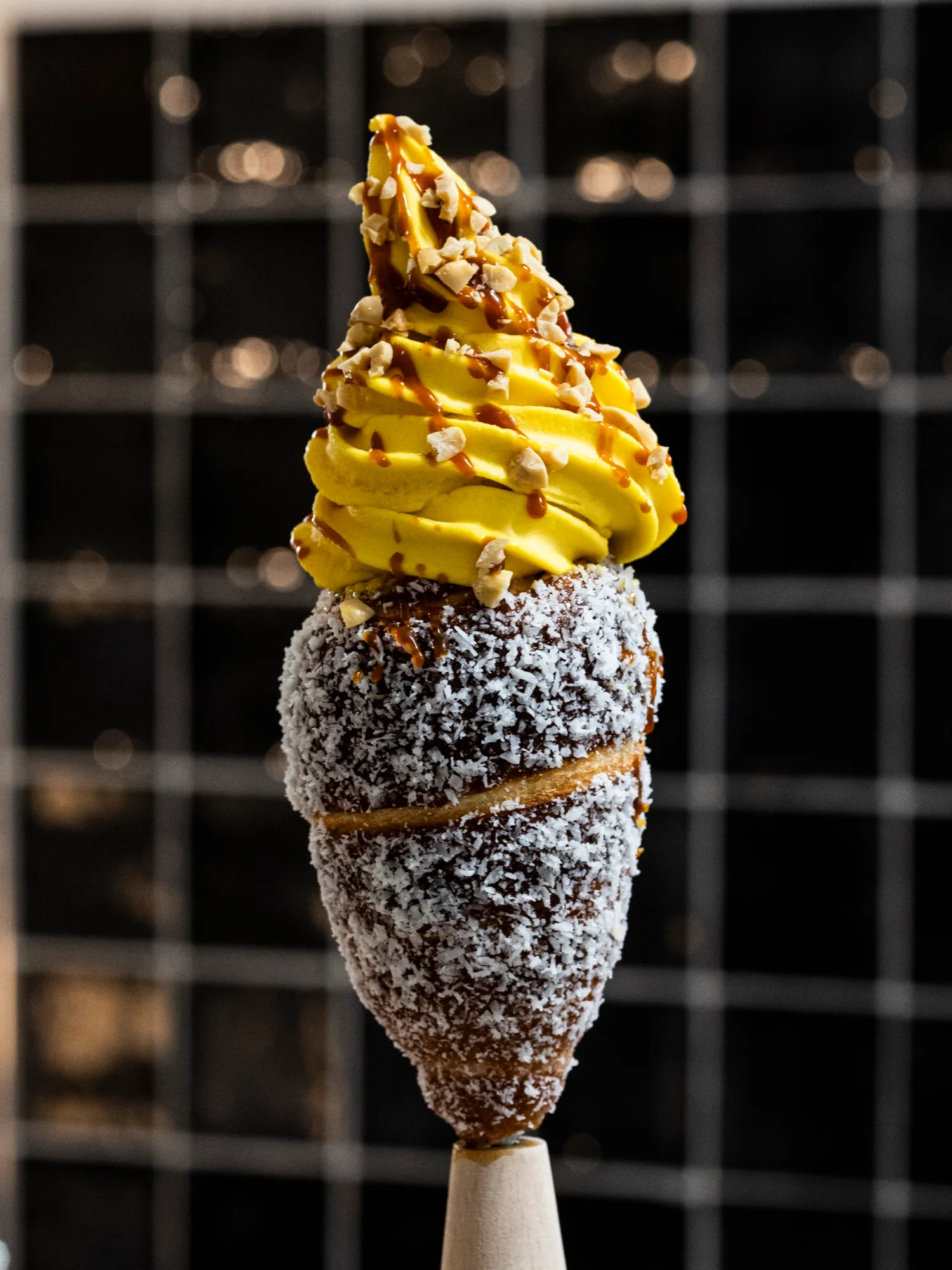 A coconut-coated chimney cone filled with mango gelato, drizzled with caramel and peanuts