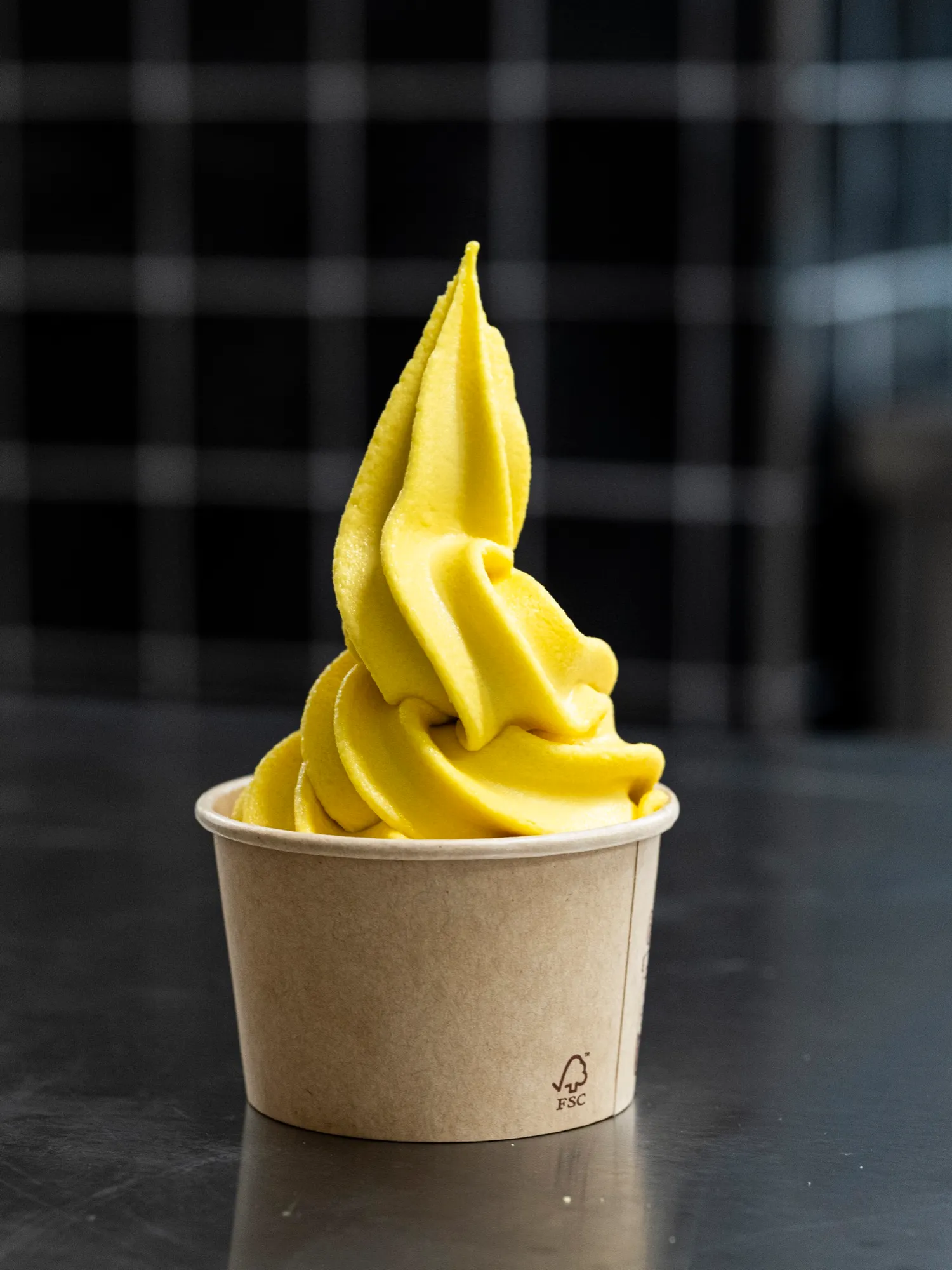 A swirl of bright yellow mango gelato in a kraft paper cup
