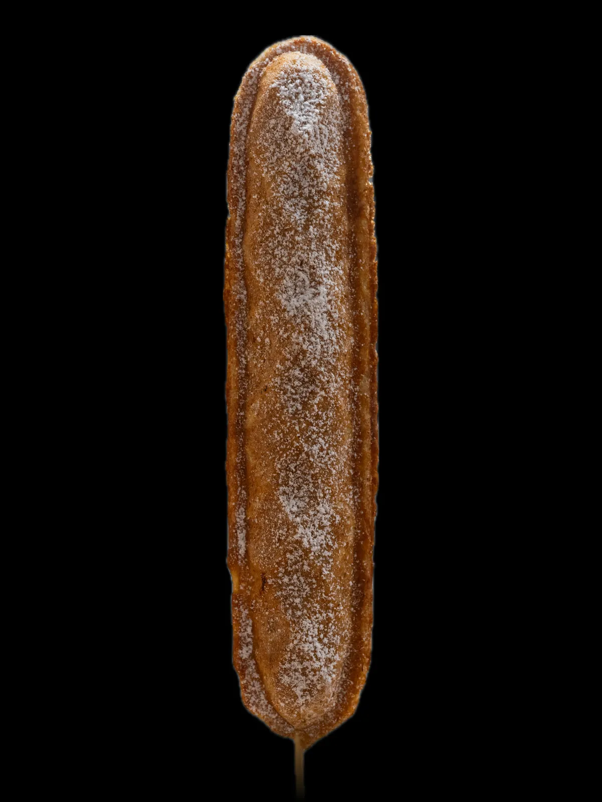 A long waffle on a stick with banana baked inside, dusted with sugar