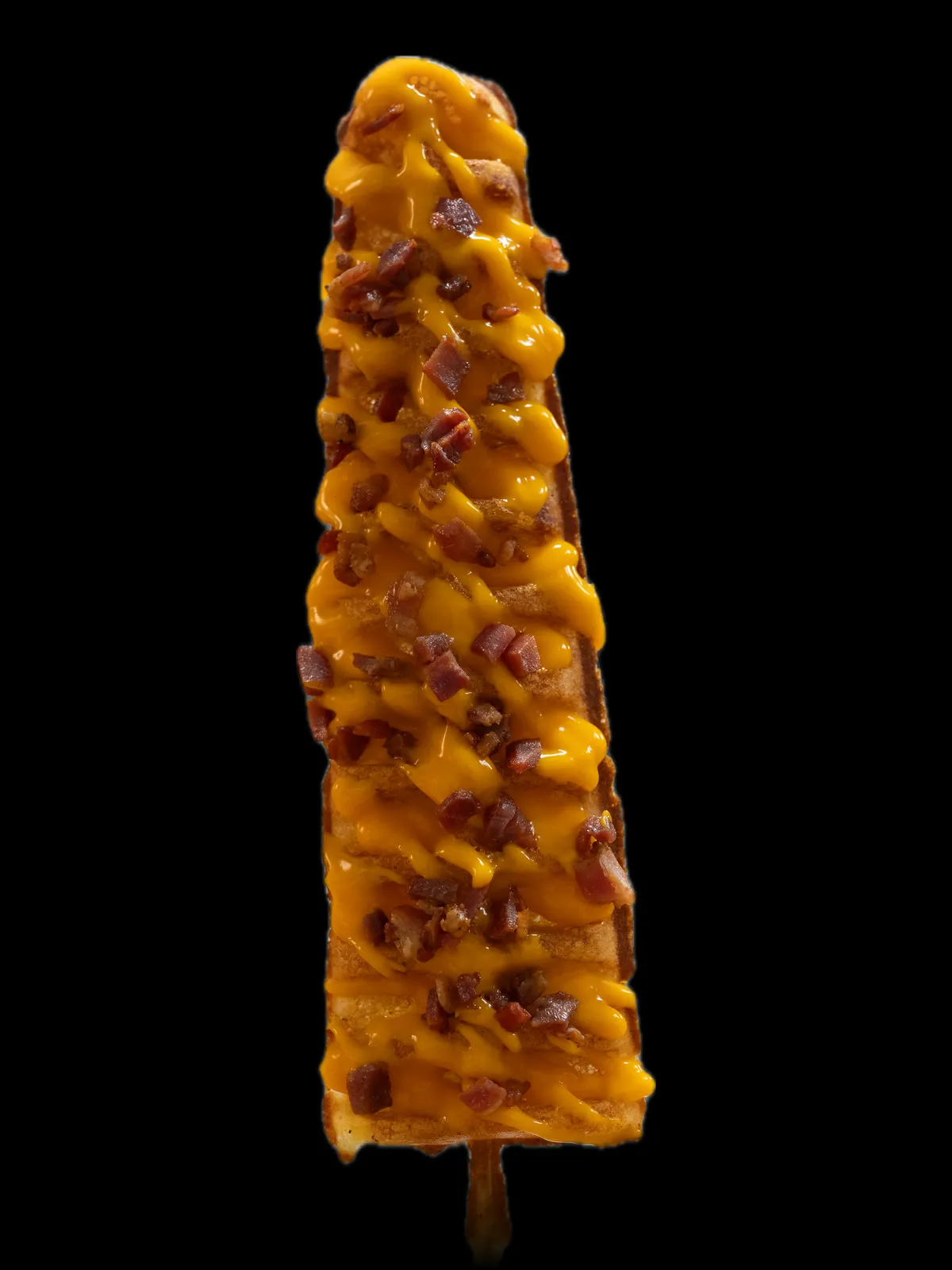 A waffle on a stick with cheese sauce and bacon pieces