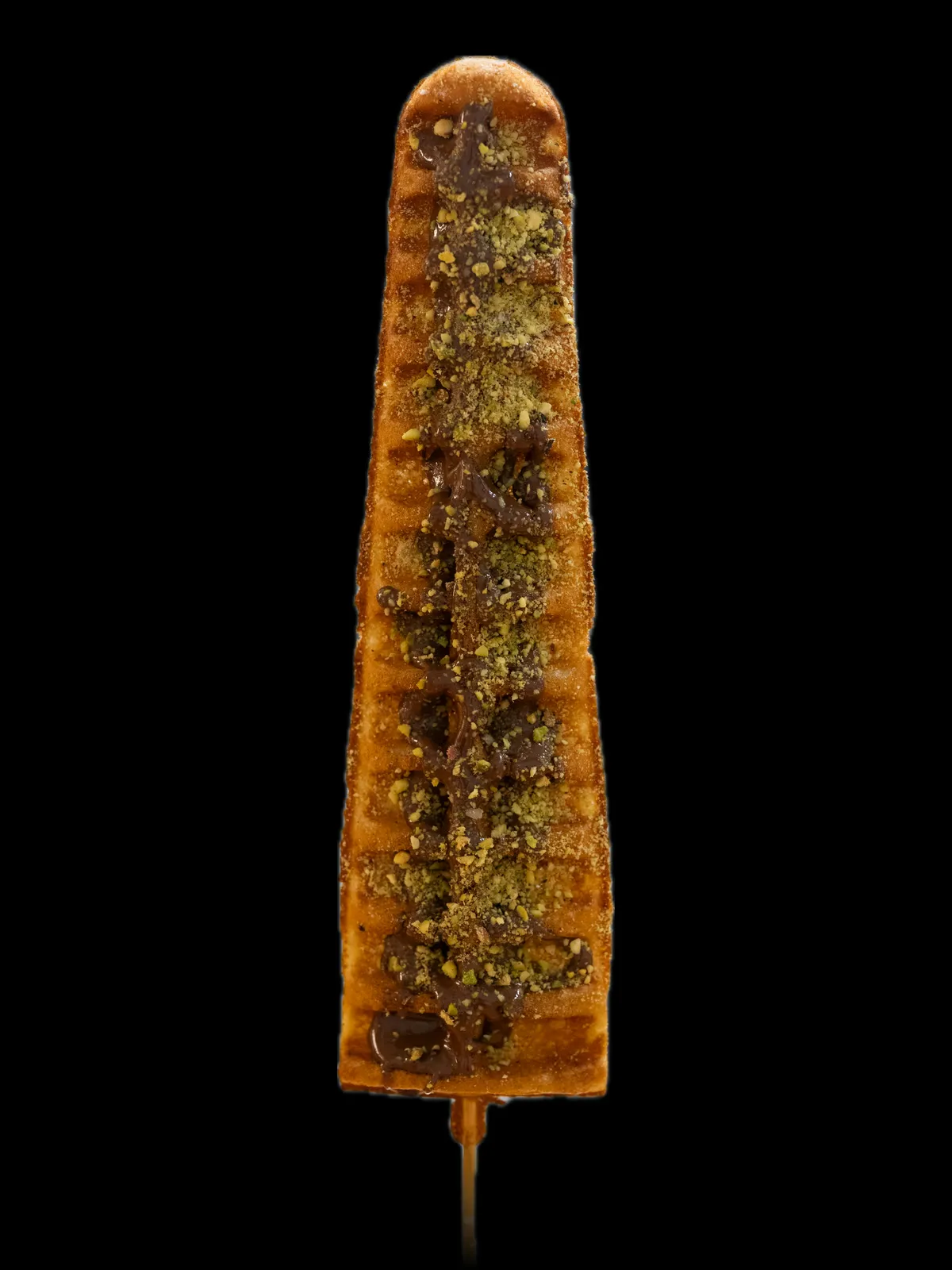 A waffle on a stick with Nutella and crushed pistachios